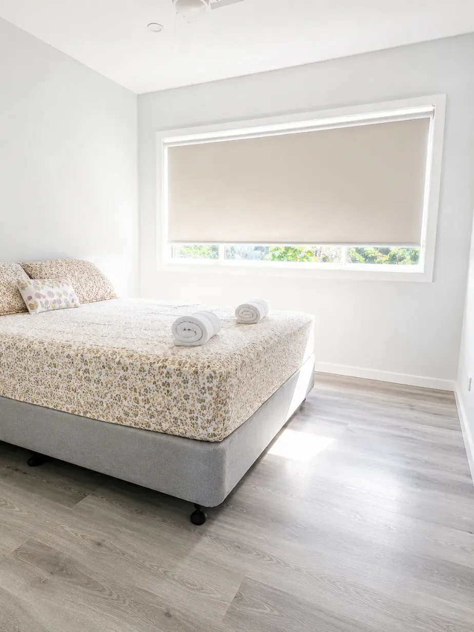 Bedroom with queen bed, floral bedspread and a wide window fitted with a roller blind