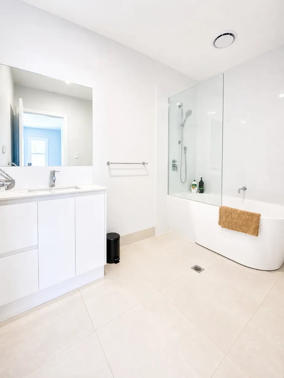 Bathroom with white vanity, wide mirror, glass-screened shower and freestanding bath