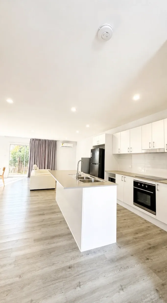 Kitchen with white cabinetry, island bench, stainless steel sink and under-bench oven