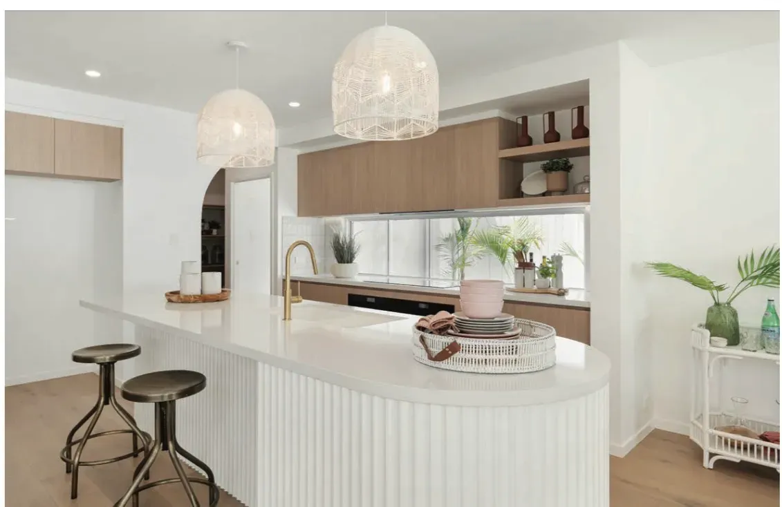White and timber kitchen with a curved island bench, pendant lighting and gold tapware